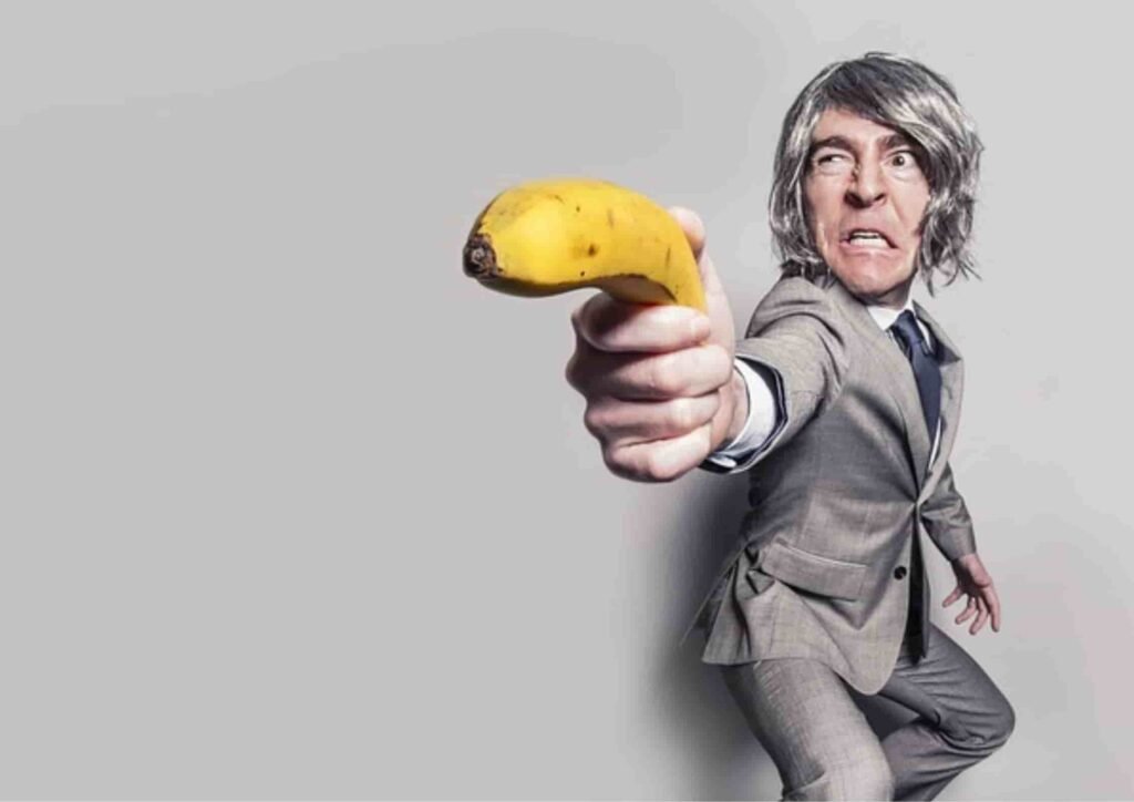 A suited individual points a banana towards the camera, creating a humorous and playful scene against a plain background.