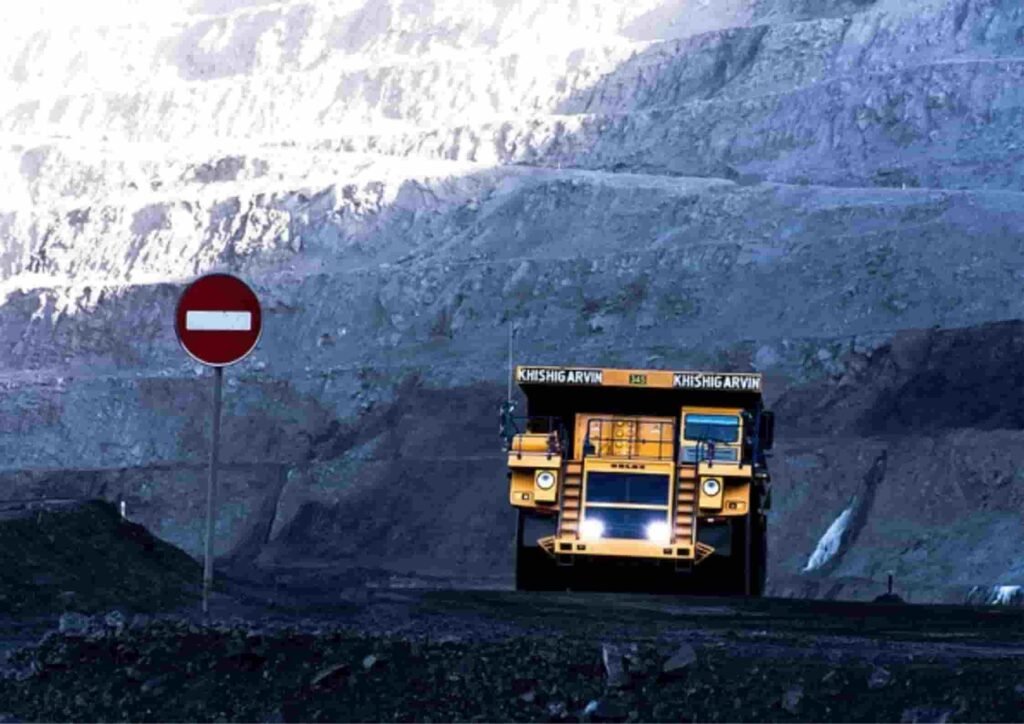 A large yellow mining truck approaches a no entry sign, set against a rugged, earthy landscape of deep mine walls.